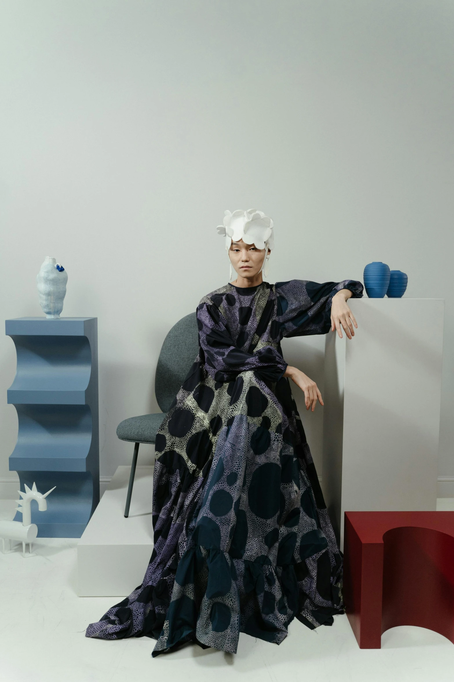 a woman sitting on a chair in a room, a surrealist sculpture, inspired by Gao Cen, unsplash, maximalism, wearing long gown, blue and gray colors, off - white collection, an oversized beret