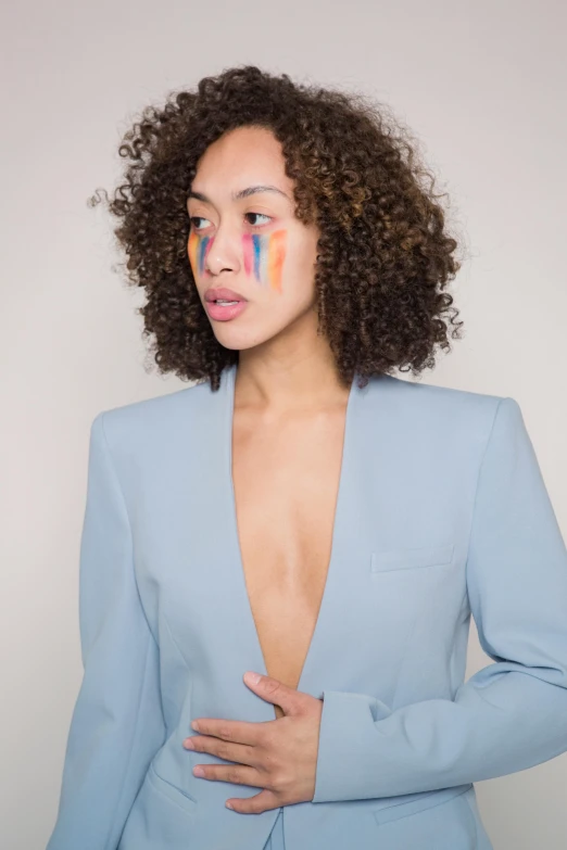 a woman in a blue suit with paint on her face, an album cover, inspired by Louis Le Nain, trending on pexels, curly haired, roygbiv, light skin, blue skintight closed longcoat