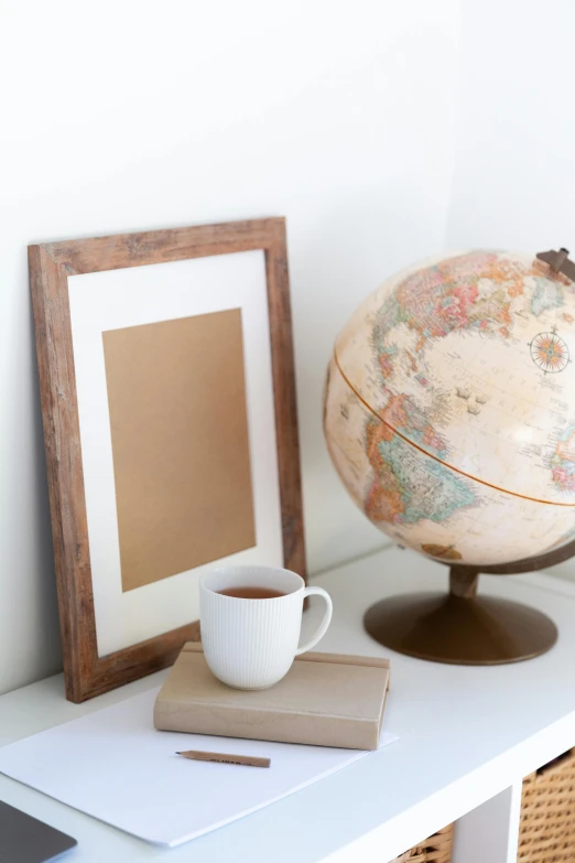 a white table topped with a globe and a cup of coffee, visual art, card frame, full product shot, vintage photo, short bookshelf