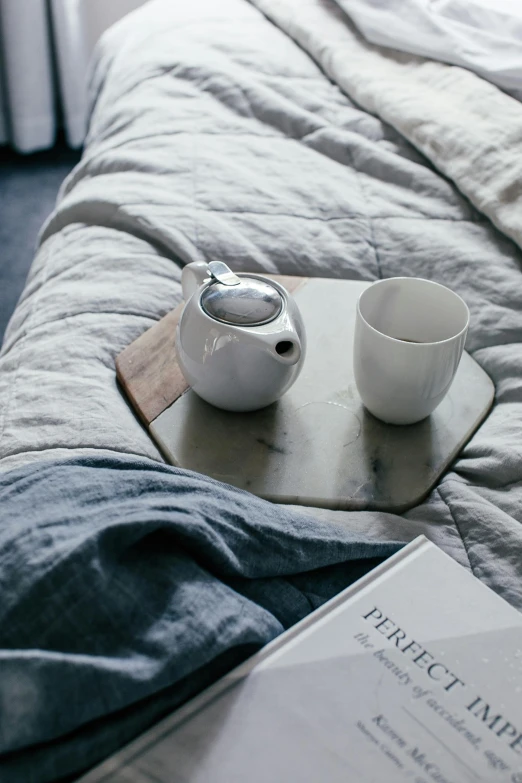 a book sitting on top of a bed next to a cup of coffee, inspired by Bedwyr Williams, minimalism, teapots, slate, polished white marble, bedhead
