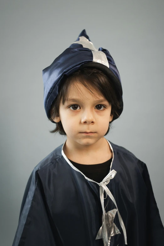 a young boy wearing a blue hat and tie, an album cover, inspired by Lucas van Leyden, shutterstock contest winner, surgical gown and scrubs on, tense look, taken in the late 2010s, dark blue cape