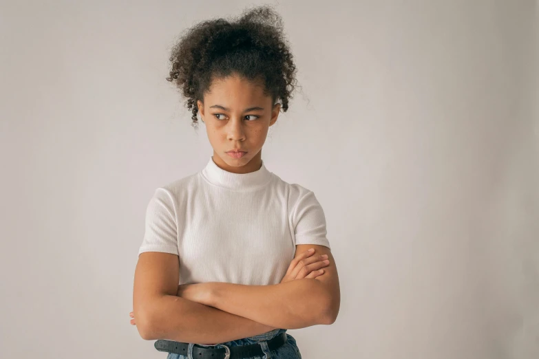 a young girl standing with her arms crossed, trending on pexels, antipodeans, mixed race, frowning, in white turtleneck shirt, wearing a tee shirt and combats