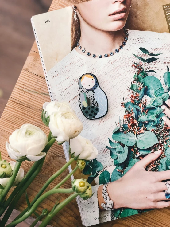 a magazine sitting on top of a wooden table, a picture, by Julia Pishtar, cloisonnism, lady with glowing flowers dress, puffy sticker, style of julia razumova, luxurious neckless