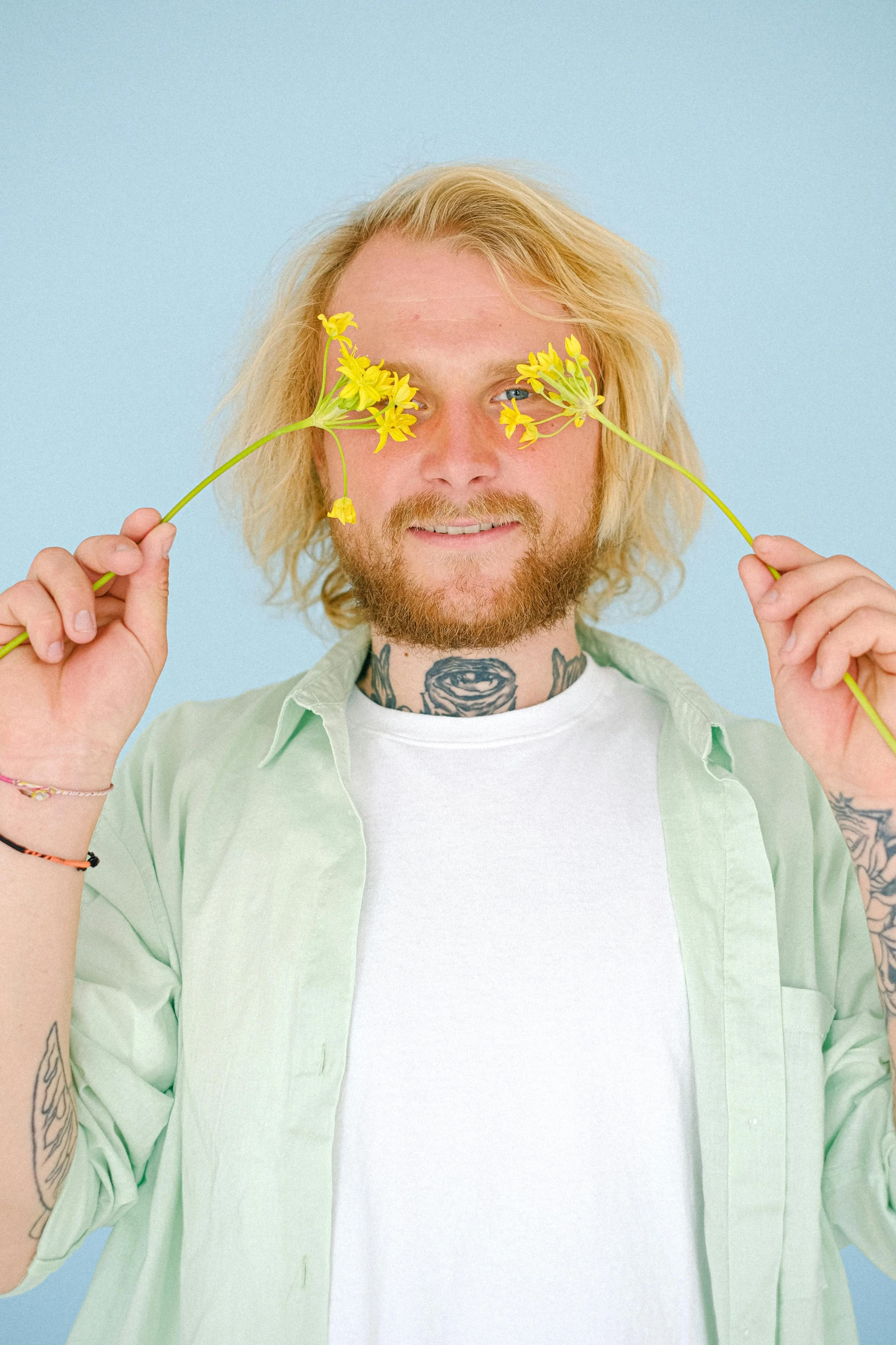 a man holding flowers in front of his face, an album cover, inspired by Lasar Segall, trending on pexels, light yellow hair, tattoos, giddy smirk, studio portrait