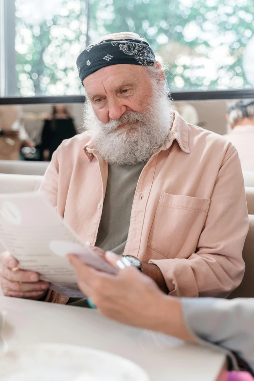 a man sitting at a table reading a newspaper, by Daren Bader, pexels contest winner, renaissance, overalls and a white beard, caring fatherly wide forehead, sitting in a waiting room, gif