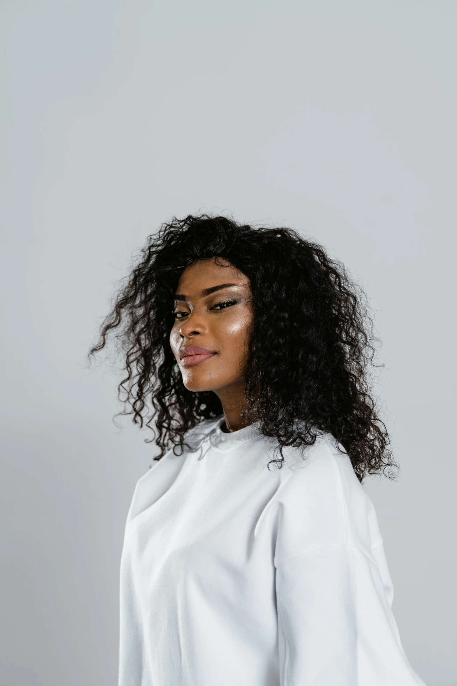 a woman wearing a white shirt and black pants, an album cover, by Lily Delissa Joseph, trending on pexels, curls hair, hair texture, wearing a black hoodie, plain background