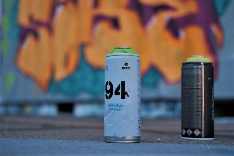 a can of spray paint next to a can of spray paint, a picture, by Naza, unsplash, graffiti, 9 9 designs, 1894, 4l, far - mid shot