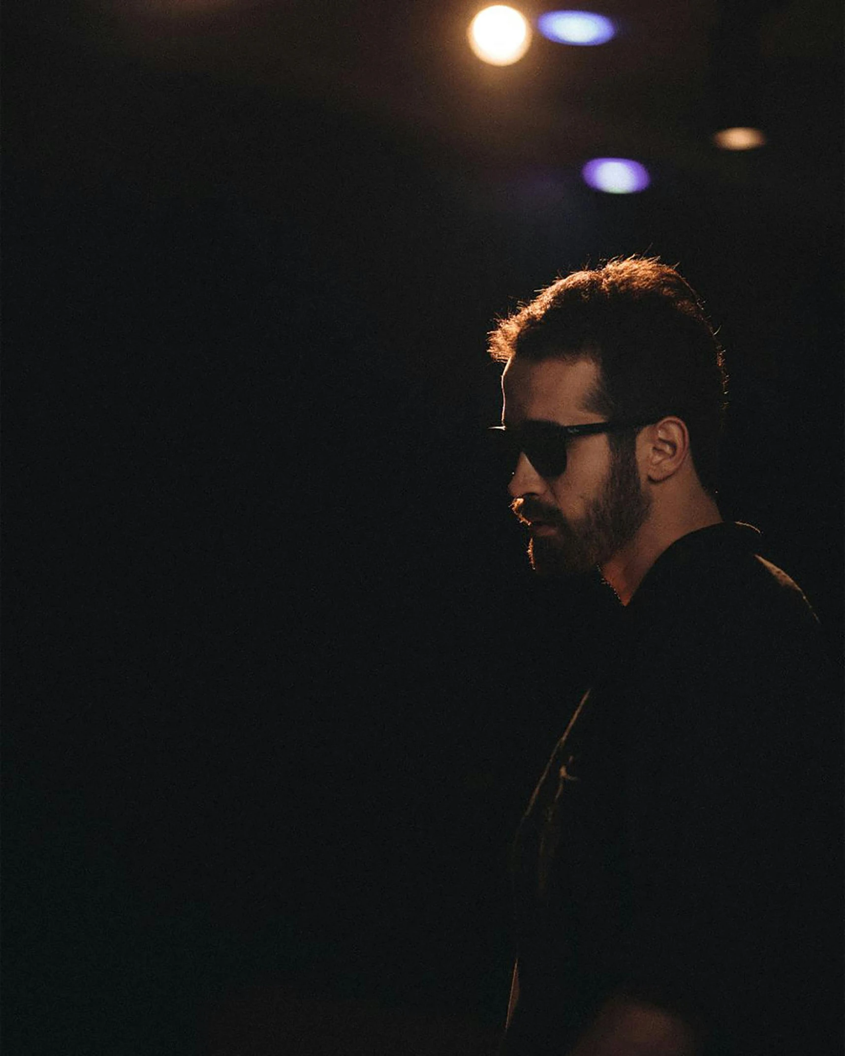 a man standing in front of a microphone in a dark room, an album cover, unsplash, hurufiyya, sunglasses, portrait of chris evans, reza afshar, slightly pixelated