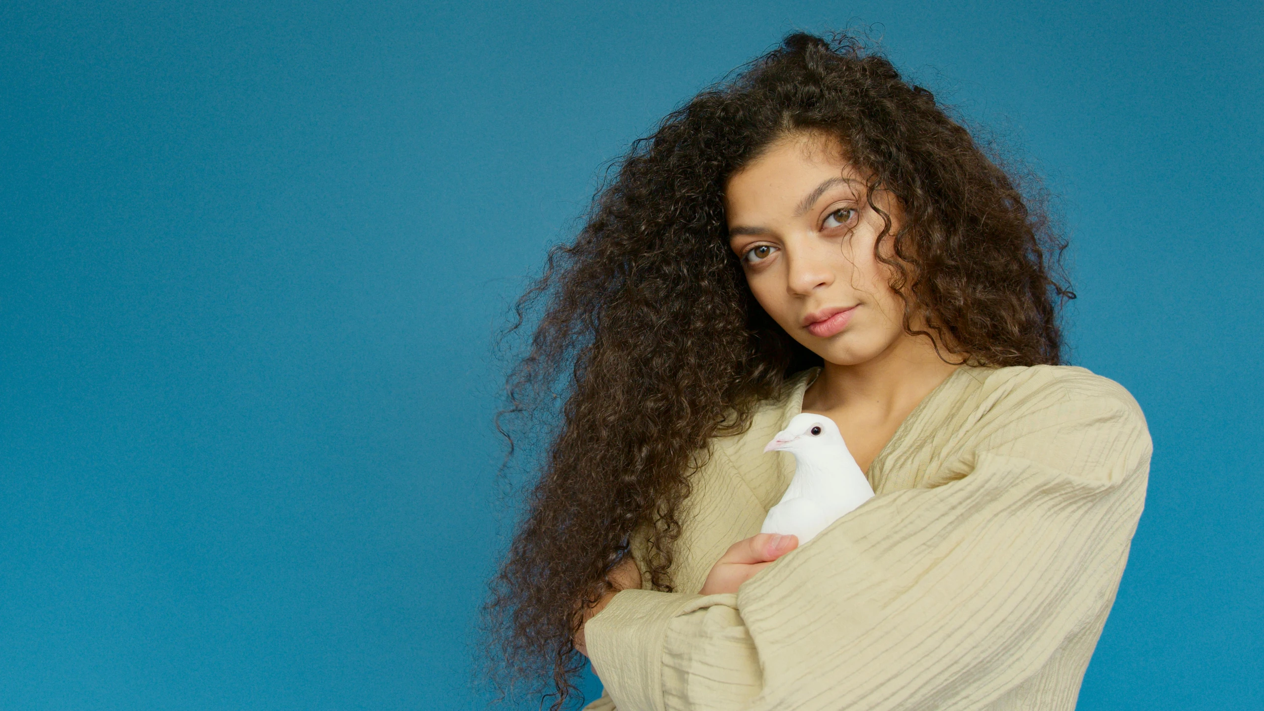 a woman holding a white bird in her arms, an album cover, inspired by Jean-Étienne Liotard, trending on pexels, long dark curly hair, charli bowater and artgeem, riyahd cassiem, press shot