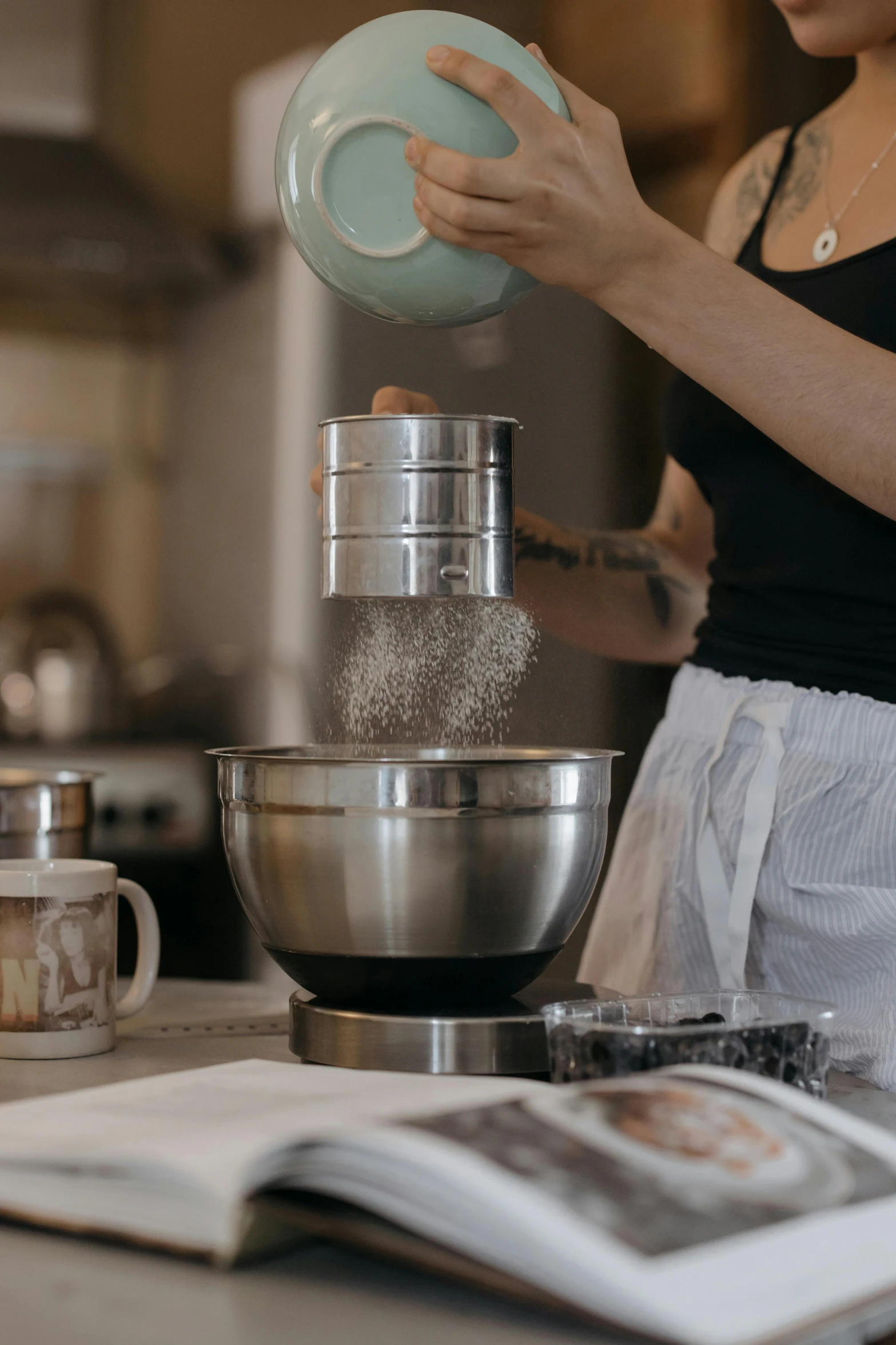 a woman pouring something into a bowl in a kitchen, trending on pexels, sand particles, stainless steel, gif, grey