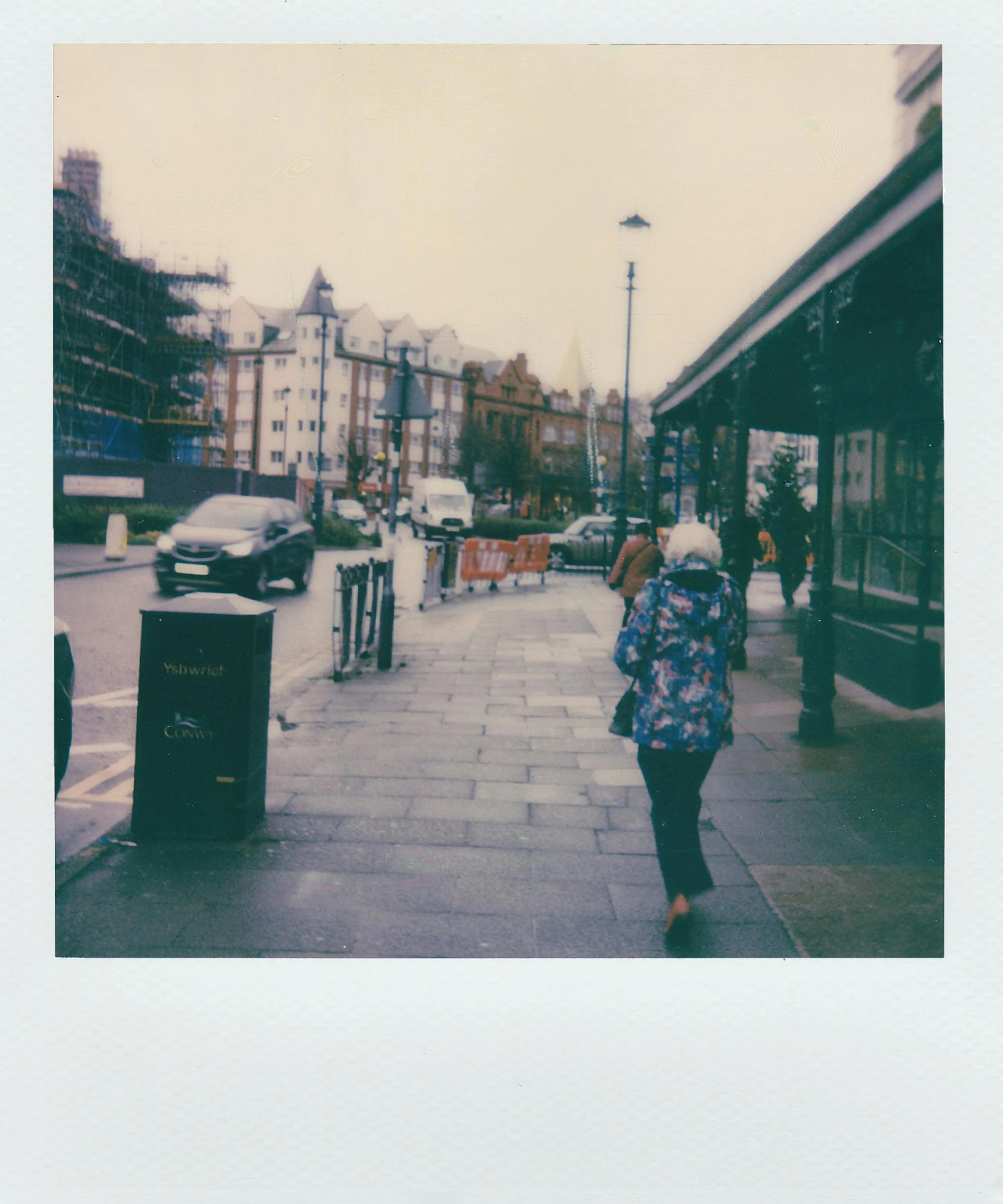 a woman walking down a sidewalk in the rain, a polaroid photo, london streets in background, in a square, blueish tones, outside on the ground