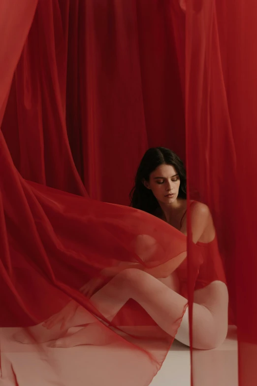 a woman sitting in front of a red curtain, showstudio, sheer fabrics, vermillion, shot with sony alpha