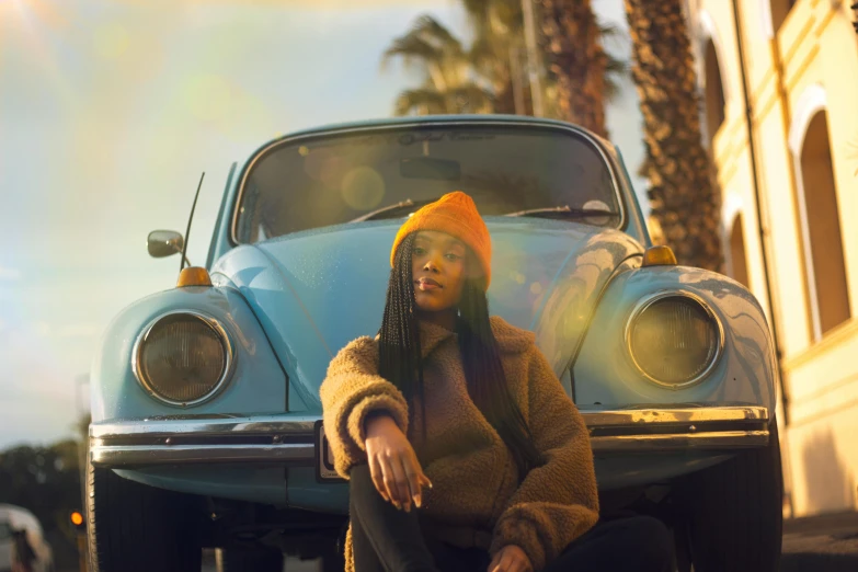 a woman sitting in front of a blue car, by mads berg, pexels contest winner, afrofuturism, willow smith zendaya, beetle, warm light, standing in front of lowrider