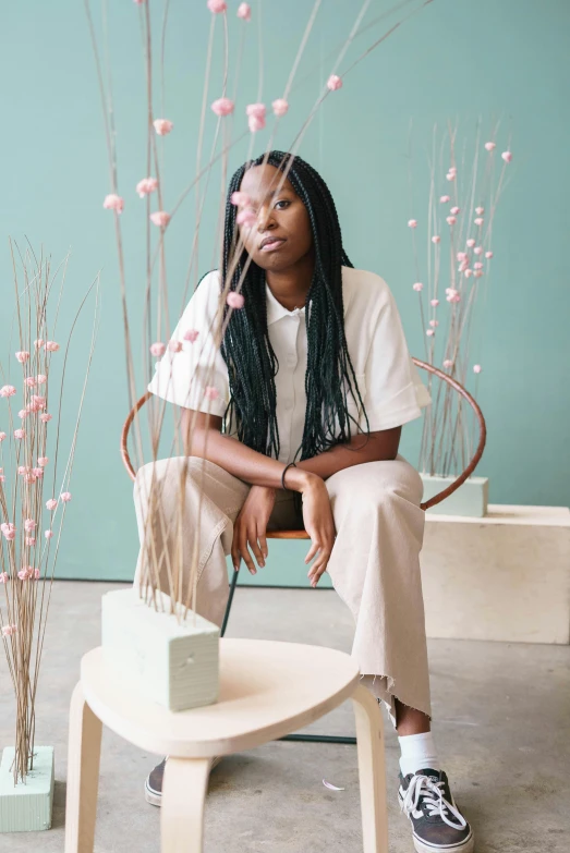 a woman sitting on top of a wooden chair, trending on unsplash, wearing off - white style, box braids, blooming, on a pale background