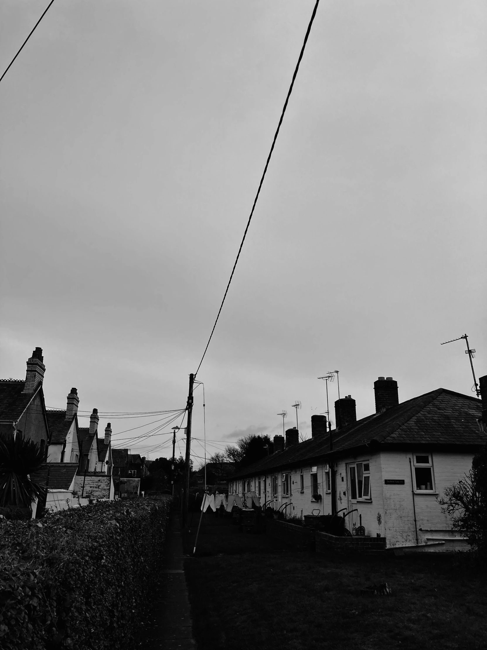 a black and white photo of a street with houses, by Dave Allsop, telephone wires, black sky, alternate album cover, cottages