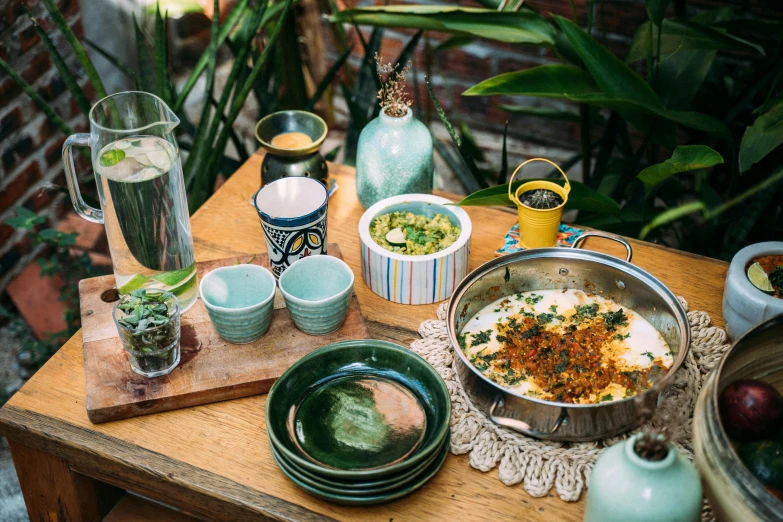 a wooden table topped with bowls of food, unsplash, cloisonnism, garden setting, cheesy, cooking oil, sea - green and white clothes