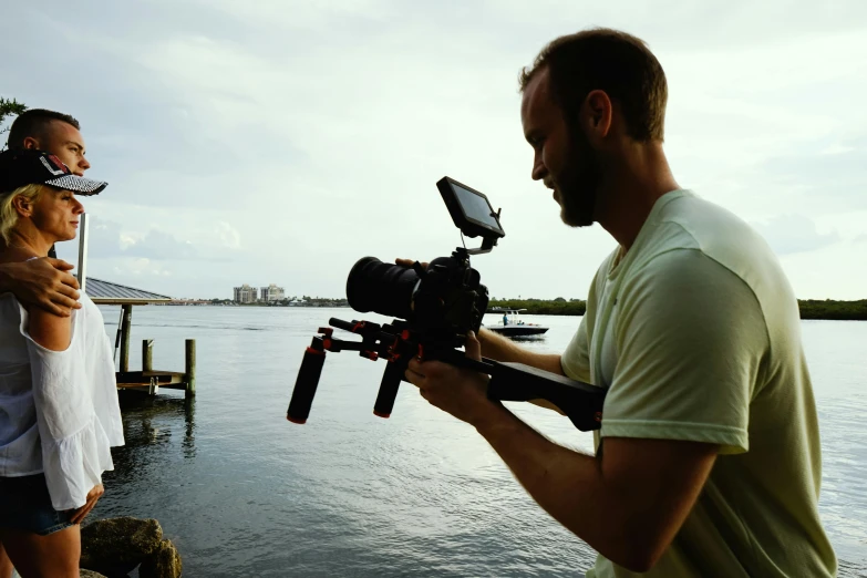 a man standing next to a woman holding a camera, unsplash, video art, low camera angle at water level, graded with davinci resolve, movie set”, casey cooke