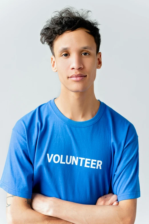 a young man standing with his arms crossed, a picture, inspired by John Luke, blue tight tshirt, official government photo, - 12p, large text