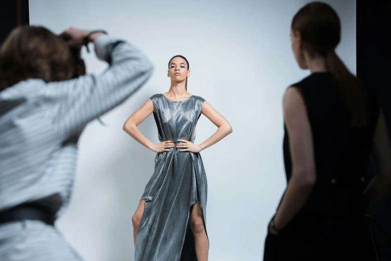 a woman taking a picture of another woman in a dress, by Adam Marczyński, pexels contest winner, photorealism, wearing silver dress, at a fashion shoot, coated pleats, various posed