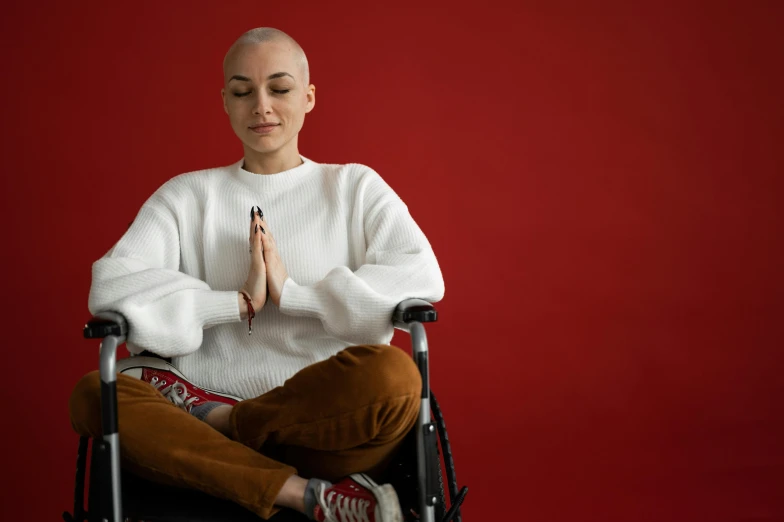 a woman in a wheelchair doing yoga on a red background, trending on pexels, antipodeans, bald head, praying, looking towards camera, on a gray background