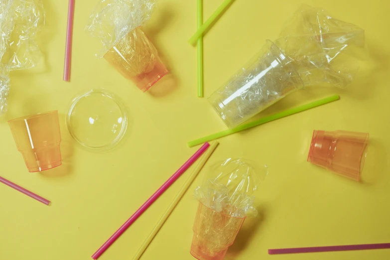 a bunch of plastic straws sitting on top of a table, an album cover, trending on pexels, plasticien, yellow backdrop, jelly glow, cups and balls, cracked plastic wrap