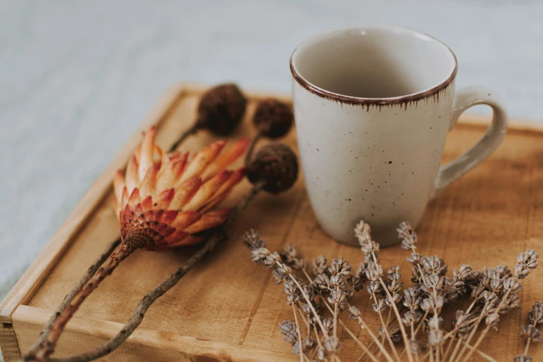 a coffee cup sitting on top of a wooden tray, a still life, trending on pexels, dried flowers, with a white mug, background image, carefully crafted