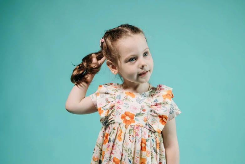 a little girl standing in front of a blue background, inspired by Elsa Beskow, pexels contest winner, dressed in a flower dress, hair in pigtails, photoshoot for skincare brand, in an action pose