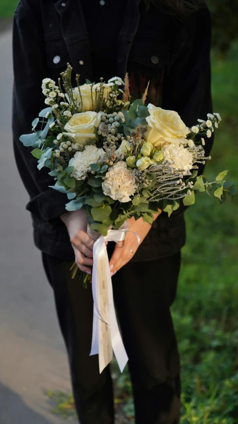 a woman standing on the side of a road holding a bouquet, pale greens and whites, shades of gold display naturally, with a black dark background, white ribbon