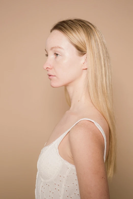 a woman standing in front of a brown wall, by Grace Clements, trending on pexels, soft pale golden skin, bust with a very long neck, in front of white back drop, perfect human female specimen