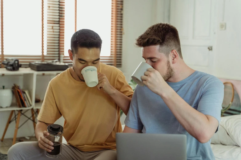 a couple of men sitting on top of a bed next to each other, pexels, is ((drinking a cup of tea)), programming, aussie baristas, cute boys