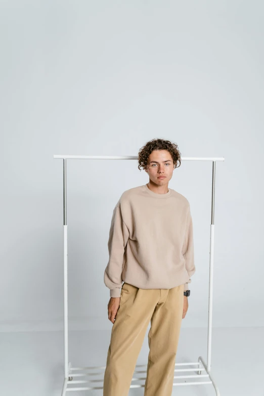 a man standing in front of a white frame, inspired by Jonas De Ro, trending on unsplash, wearing an oversized sweater, light tan, male teenager, modern studio light soft colour