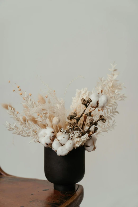 a black vase sitting on top of a wooden chair, by Winona Nelson, trending on unsplash, baroque, white flower crown, made of dried flowers, white horns, with soft bushes