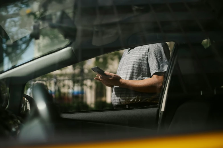 a man sitting in a car looking at his cell phone, by Carey Morris, trending on unsplash, square, wearing a modern yellow tshirt, taxis, a person standing in front of a