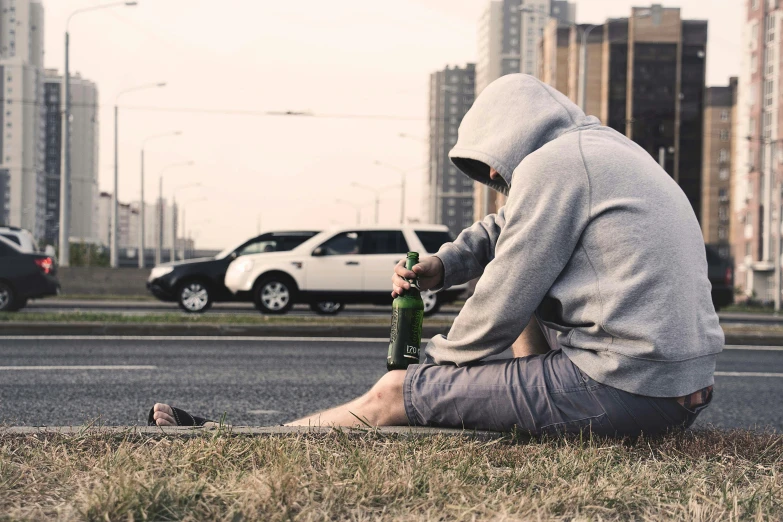 a man sitting on the side of the road with a bottle of beer, pexels contest winner, realism, gray hoodie, fighting, people resting on the grass, ptsd