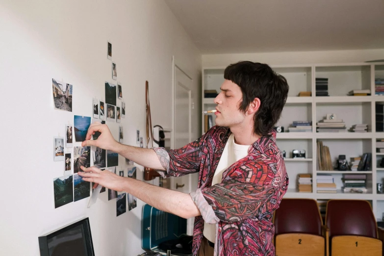 a man standing in front of a wall with pictures on it, working, home photography portrait, caleb worcester, taken on a 2010s camera