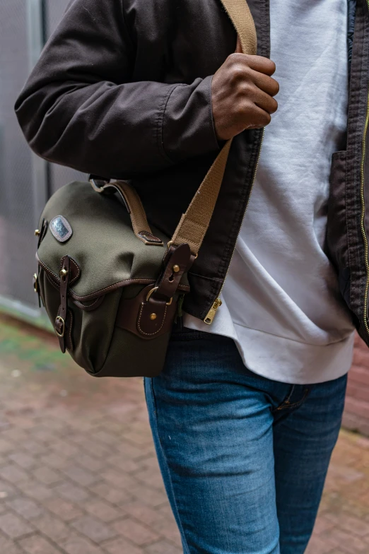 a man walking down a sidewalk carrying a bag, a picture, by Jan Tengnagel, unsplash, renaissance, wearing an ammo belt, medium format digital camera, green and brown clothes, panoramic shot