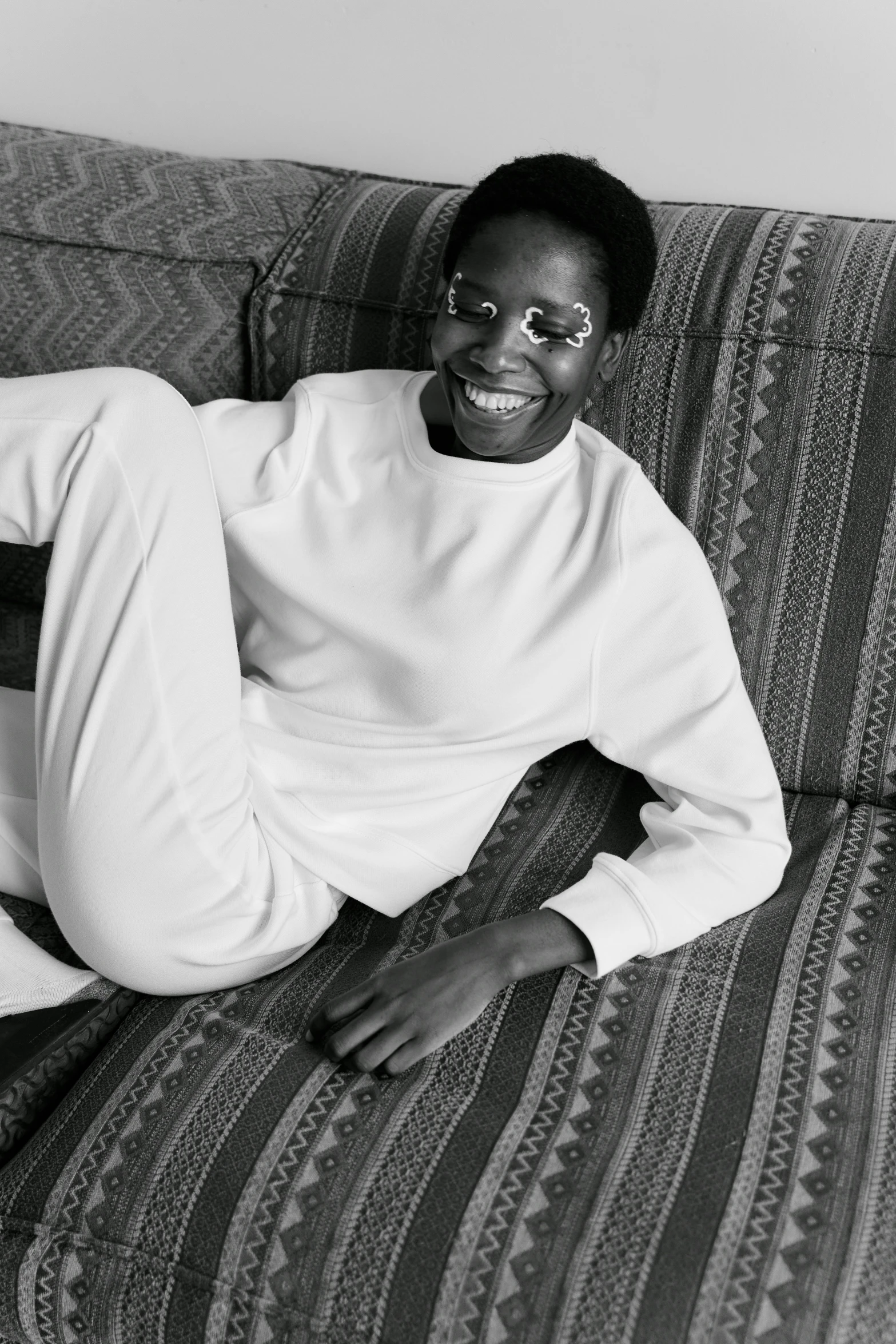 a black and white photo of a man sitting on a couch, by Maurycy Gottlieb, black teenage boy, wearing white clothes, wearing a tracksuit, androgynous male