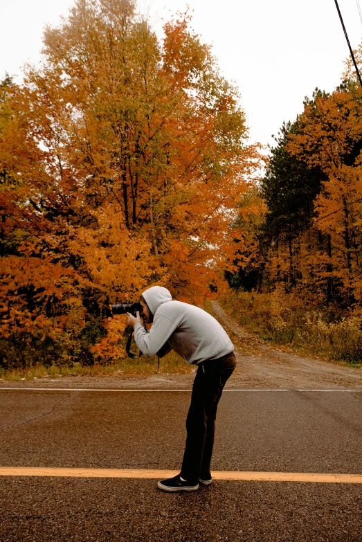 a man standing on the side of a road taking a picture, by Robert Storm Petersen, pexels contest winner, autumn color, minn, action pose, today\'s featured photograph 4k