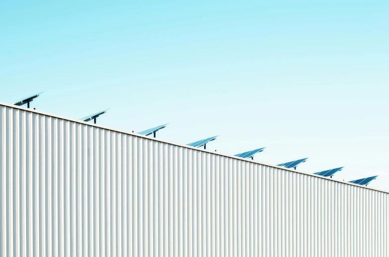 a row of solar panels on the side of a building, by Carey Morris, unsplash, postminimalism, warehouses, light blue clear sky, shot on hasselblad, pylons