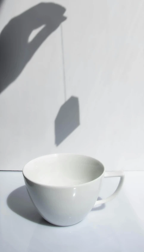 a person holding a tea bag over a cup, inspired by Suzanne Duchamp-Crotti, unsplash, conceptual art, long cast shadows, white light, silhouette :7, porcelain forcefield