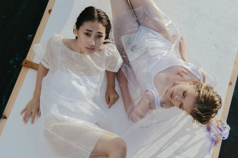 a couple of women laying on top of a bed, inspired by Ren Hang, trending on pexels, gutai group, wearing a wet white short dress, mesh fabrics, transparent, promotional image