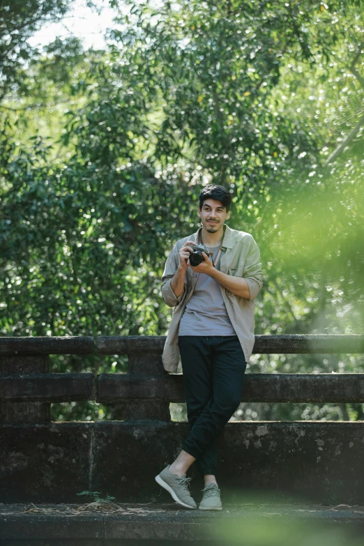 a man standing on a bridge looking at his cell phone, a picture, unsplash, happening, greenery, holding a dslr camera, australian, mid-shot of a hunky