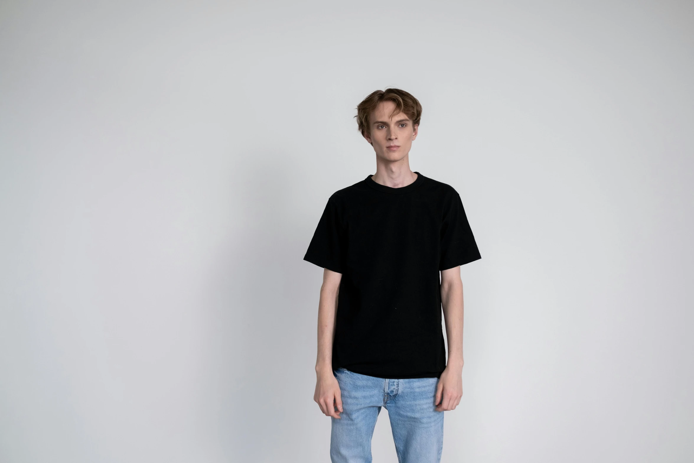 a man standing in front of a white wall, unsplash, black t shirt, detailed product image, ignant, 165 cm tall