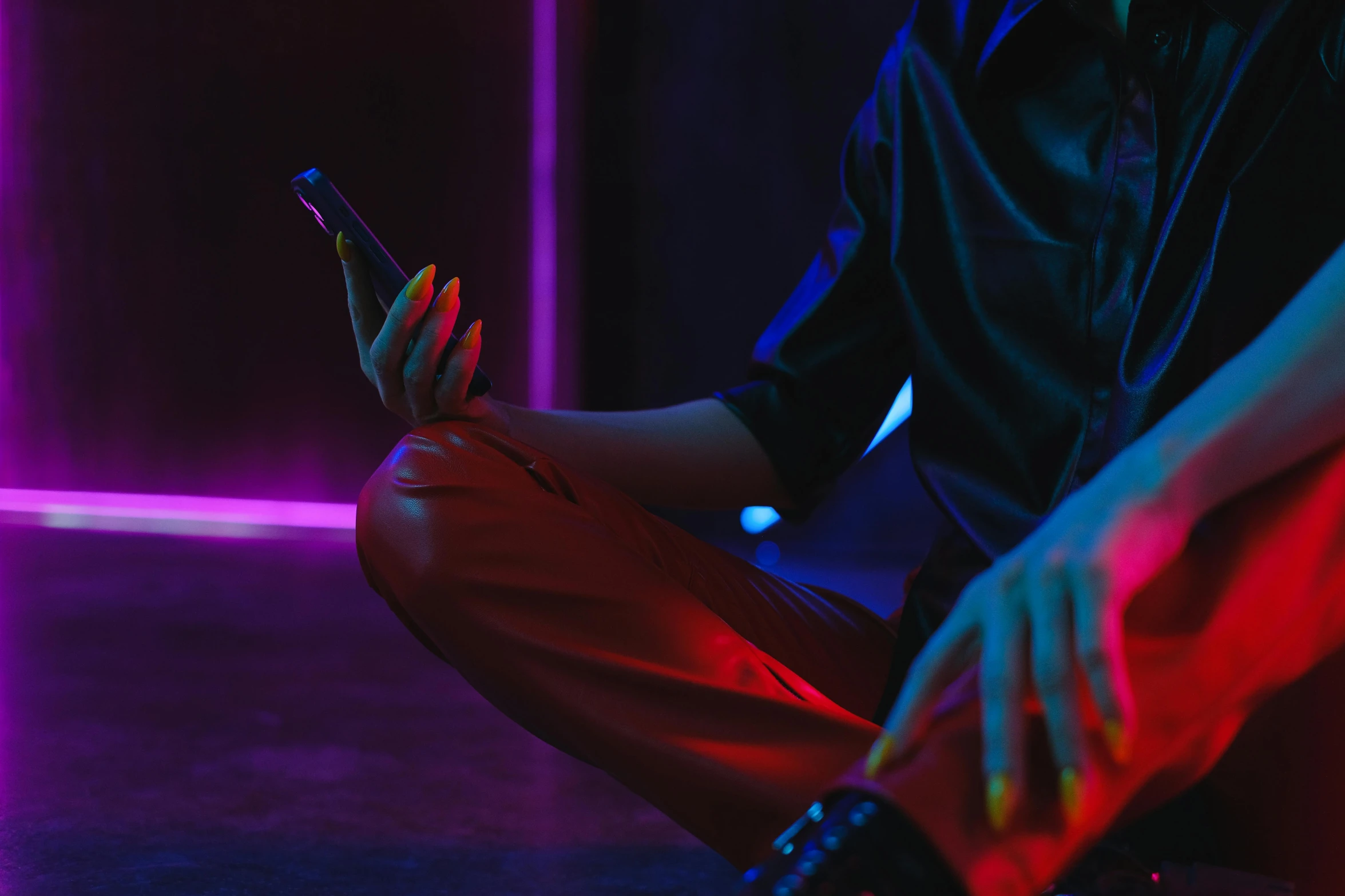 a person sitting on the ground using a cell phone, in a strip club, muted neon colors, red and obsidian neon, cyber aesthetic