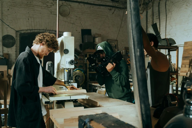 a man working on a piece of wood in a workshop, pexels contest winner, roger deakins filming, outlive streetwear collection, person in foreground, thumbnail