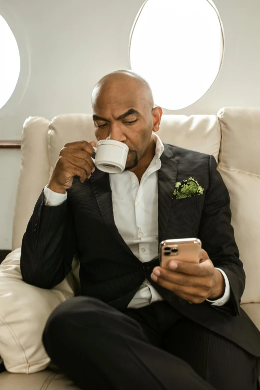 a man in a suit drinking a cup of coffee, inspired by Charles Alston, happening, aircraft, bald, looking at his phone, lounge