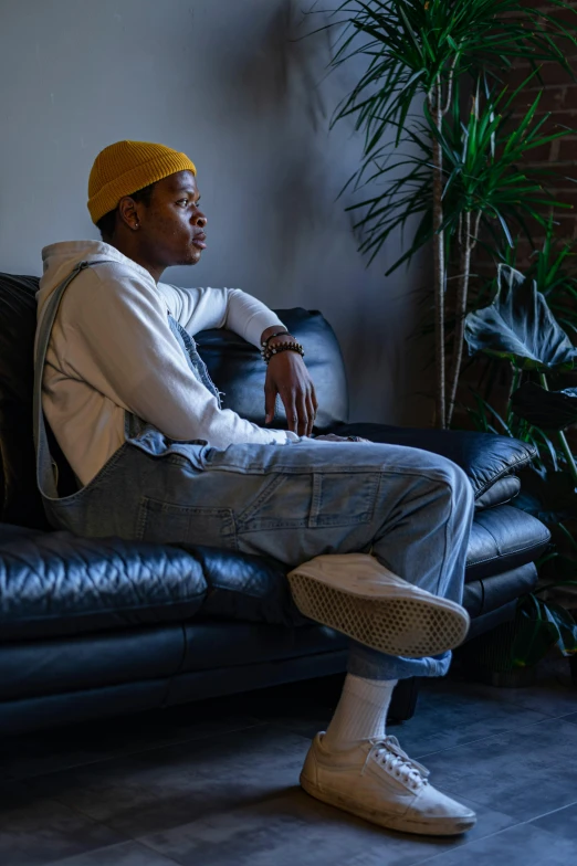 a man sitting on top of a black couch, trending on pexels, artist wearing overalls, riyahd cassiem, looking off to the side, androgynous person