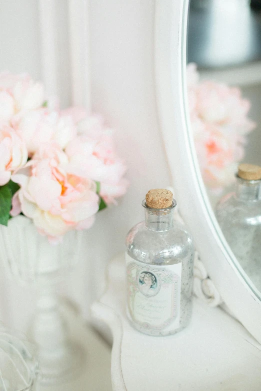 a white table topped with a vase filled with pink flowers, perfume, vintage aesthetic, tilt shift mirror background, apothecary