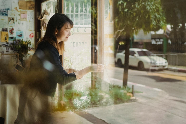 a woman looking out a window at a street, pexels contest winner, realism, exiting store, young business woman, brittney lee, nature outside