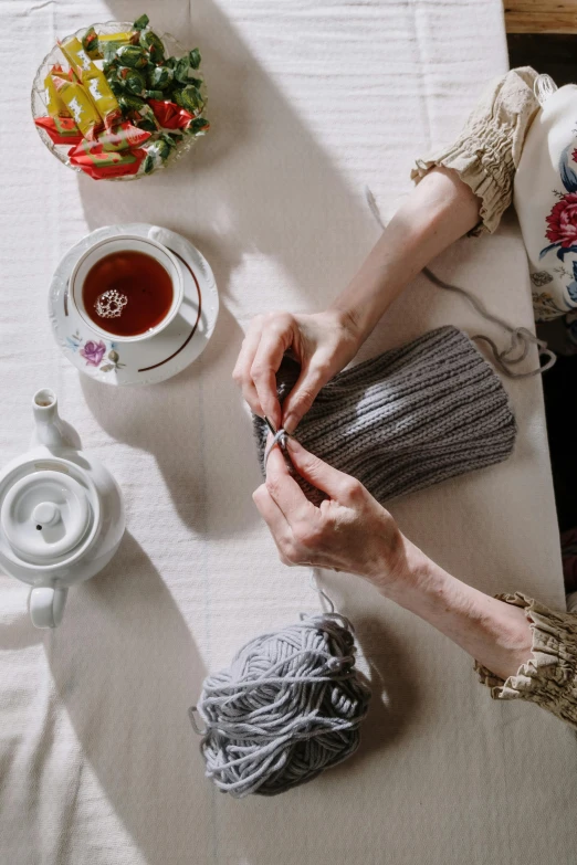 a woman sitting at a table knitting a sweater, by Elizabeth Durack, trending on pexels, tea party, grey, top down shot, sculpting